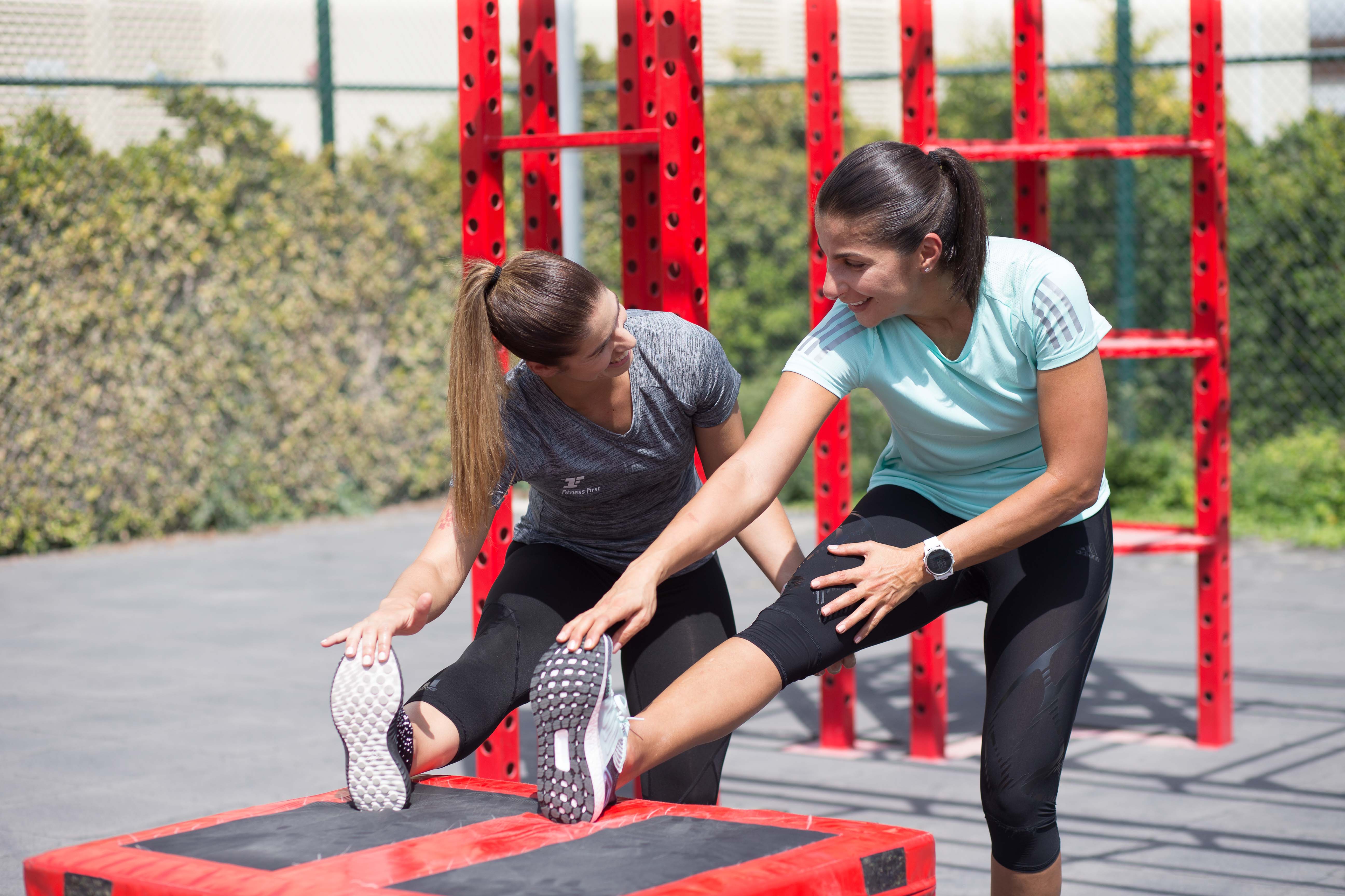 two female Fitness First members stretching in outdoor workout space two female Fitness First members stretching in outdoor workout space